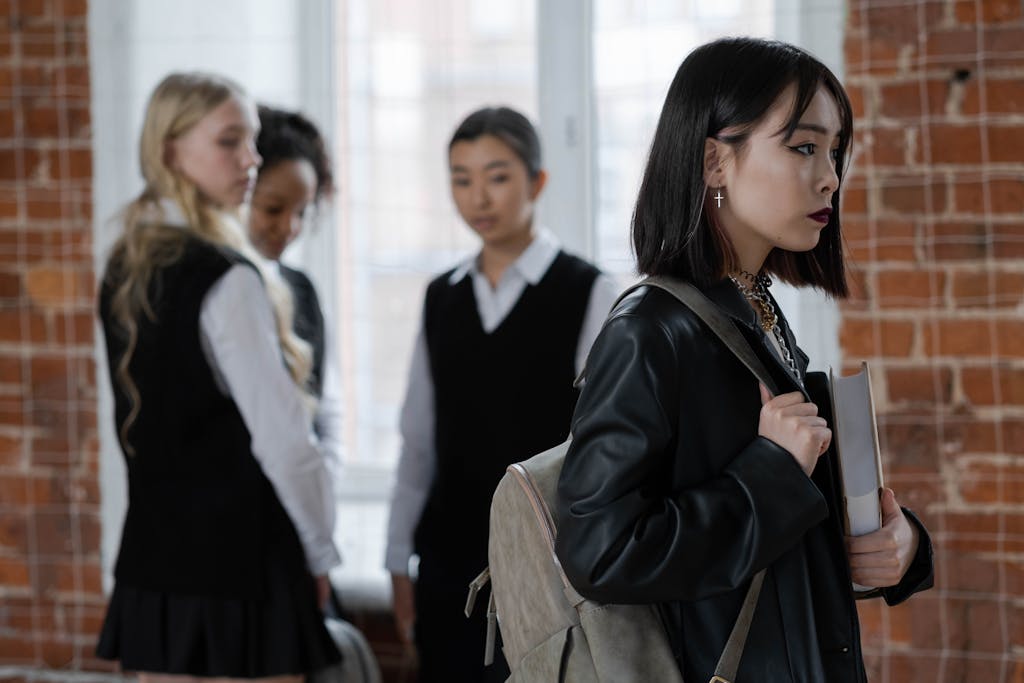 A teenage girl walks away from a group of classmates, reflecting themes of isolation and bullying.