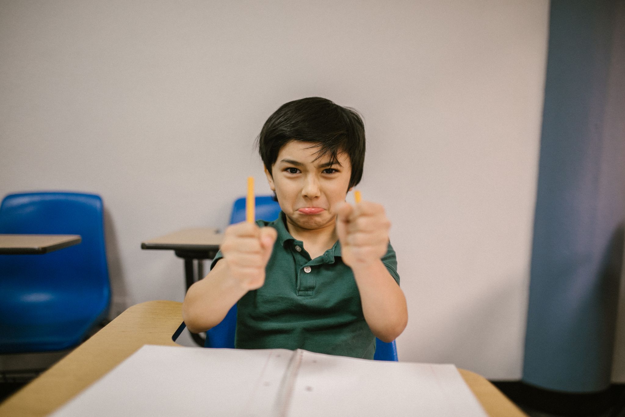 A young boy in a classroom showing frustration, holding broken pencils.