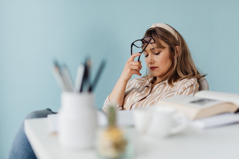 Caucasian woman looks exhausted while taking a break with eyes closed at her desk.