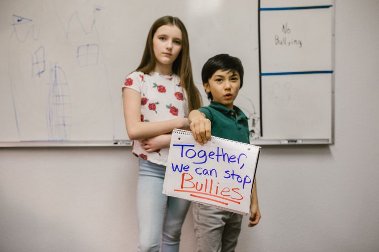Two children holding an anti-bullying sign in a classroom setting promoting awareness.