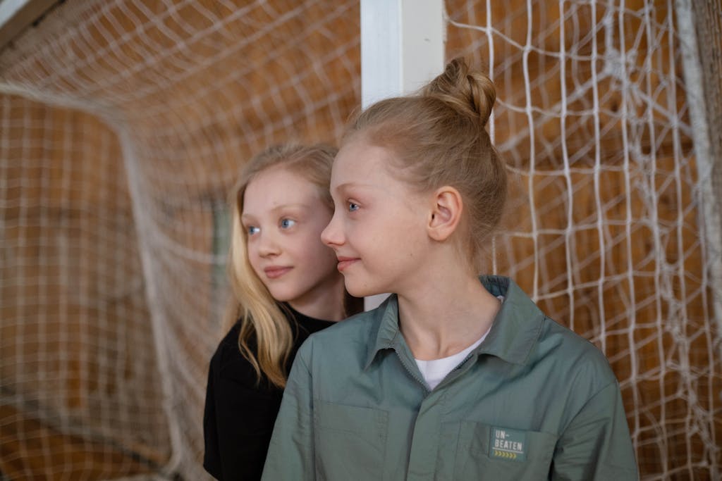 Two teenage girls standing indoors near a sports net, looking away.