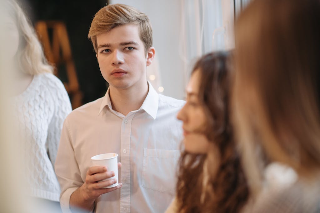 Young adult man with blond hair holding a disposable cup at a social indoor gathering.